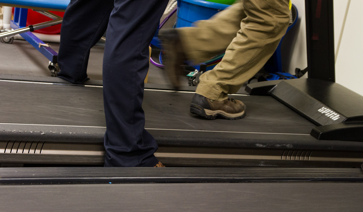 A physical therapist helping a child run on a treadmill.