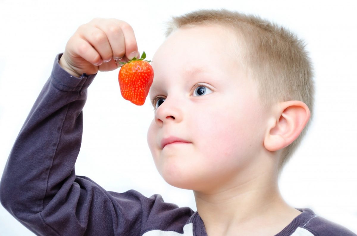 A child holding a strawberry in front of his face.