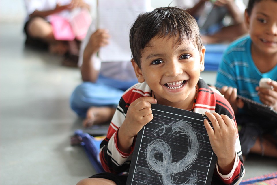 A young boy smiling with a chalkboard in a classroom.