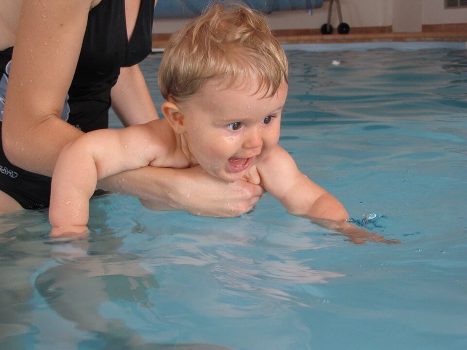 An infant being held by an adult in a swimming pool.