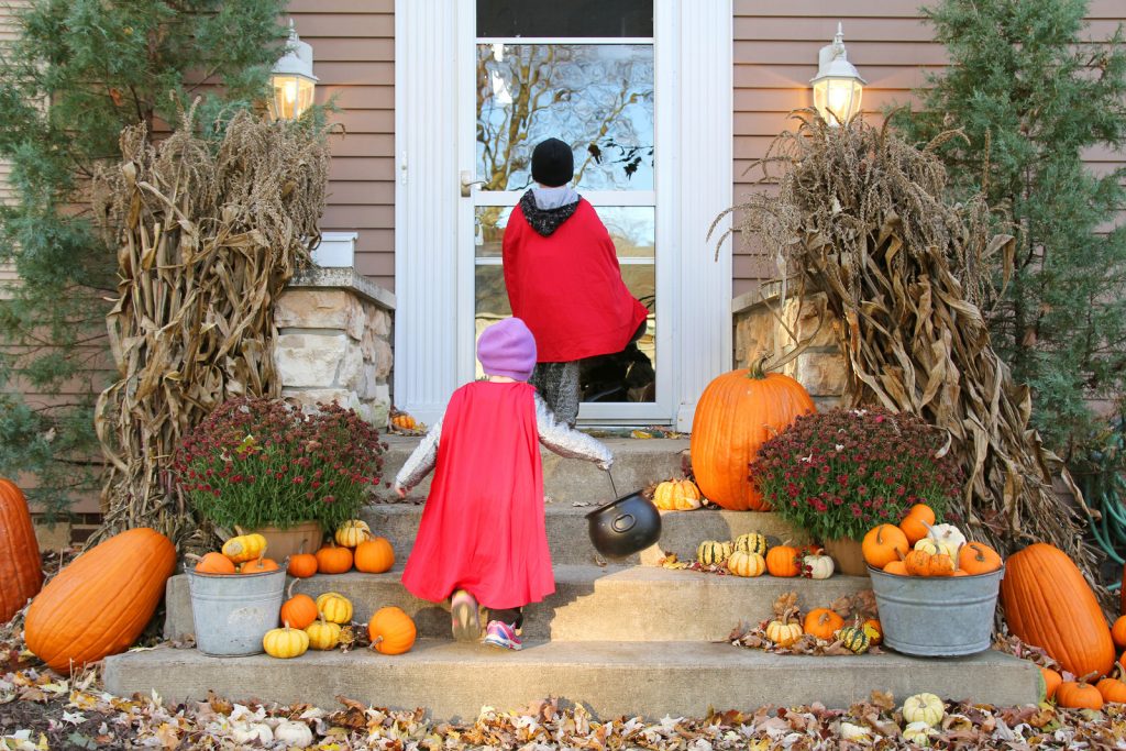 Two young children dressed up in capes for Halloween going trick-or-treating while it is still light out. 