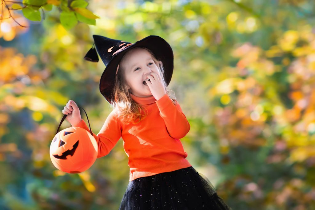 Little girl in witch costume playing in autumn park. Child having fun at Halloween trick or treat. Kids trick or treating. Toddler kid with jack-o-lantern. Children with candy bucket in fall forest.