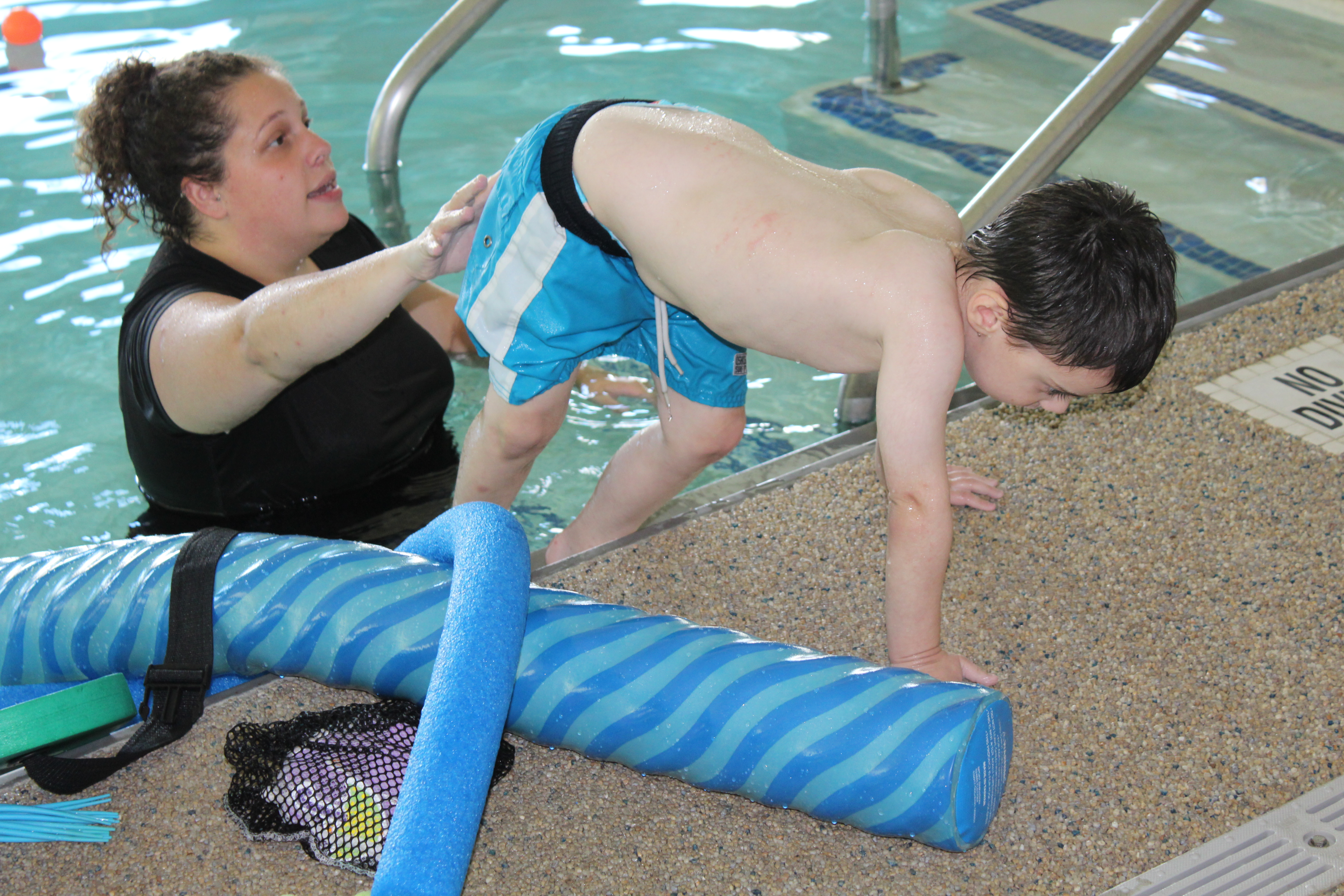 aquatic therapist working with child on strengthening lower extremity