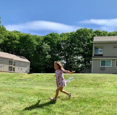 Child running in yard with hand kite