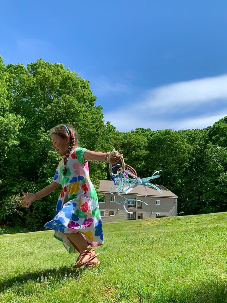 Child running in yard with hand kite