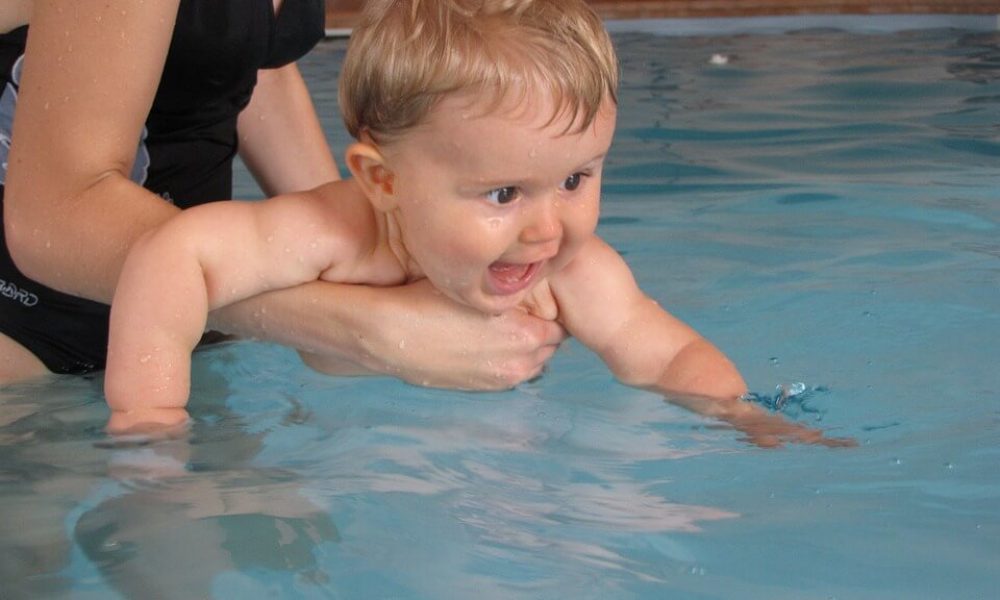 An infant being held by an adult in a swimming pool.