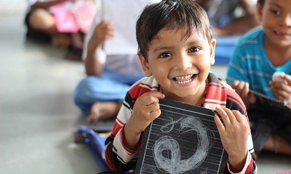 A young boy smiling with a chalkboard in a classroom.