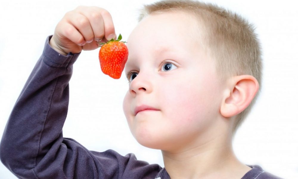 A child holding a strawberry in front of his face.